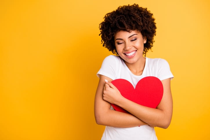a beautiful woman hugging a pillow in the shape of a heart and smiling